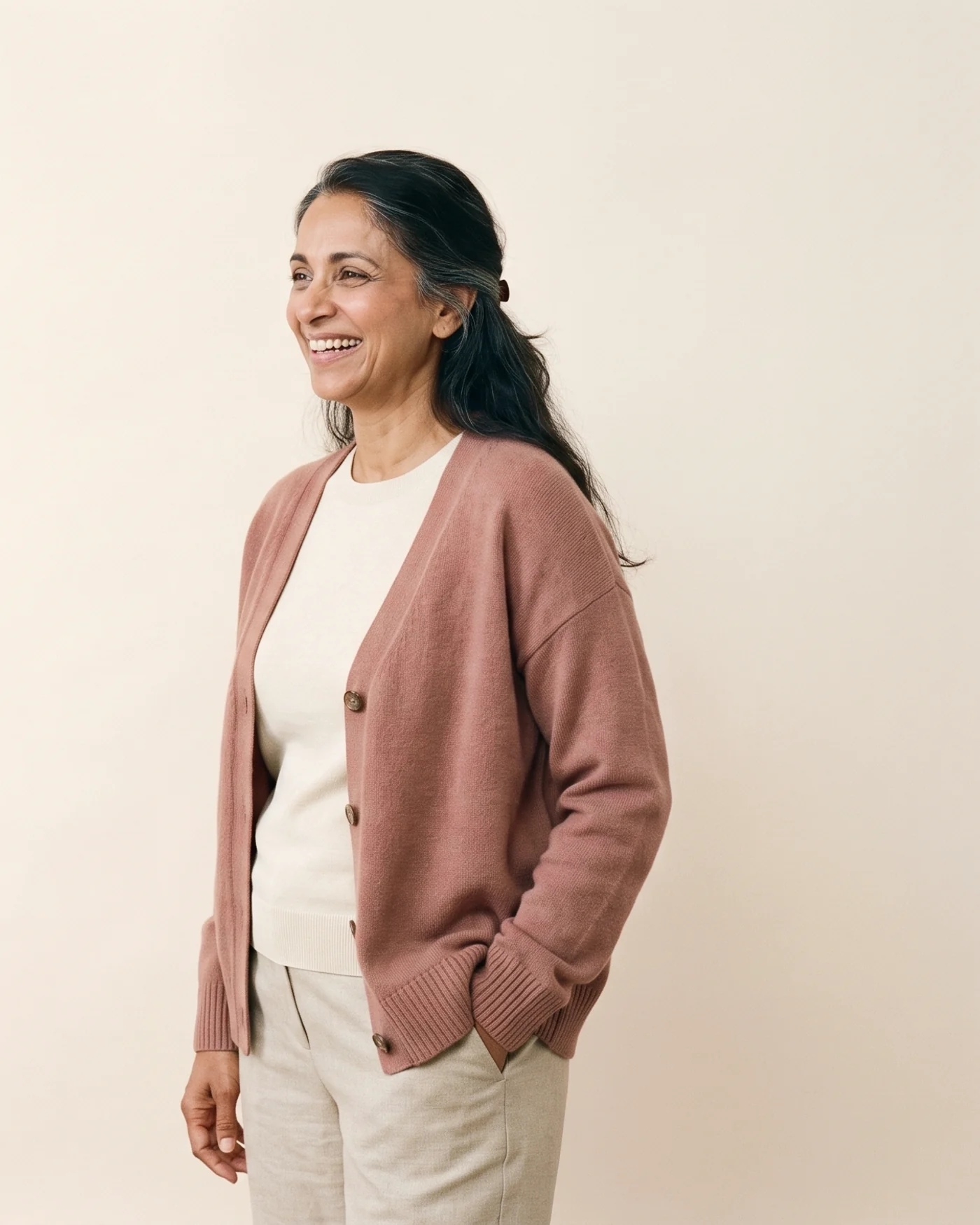 A woman in a dusty-rose cardigan laughing.