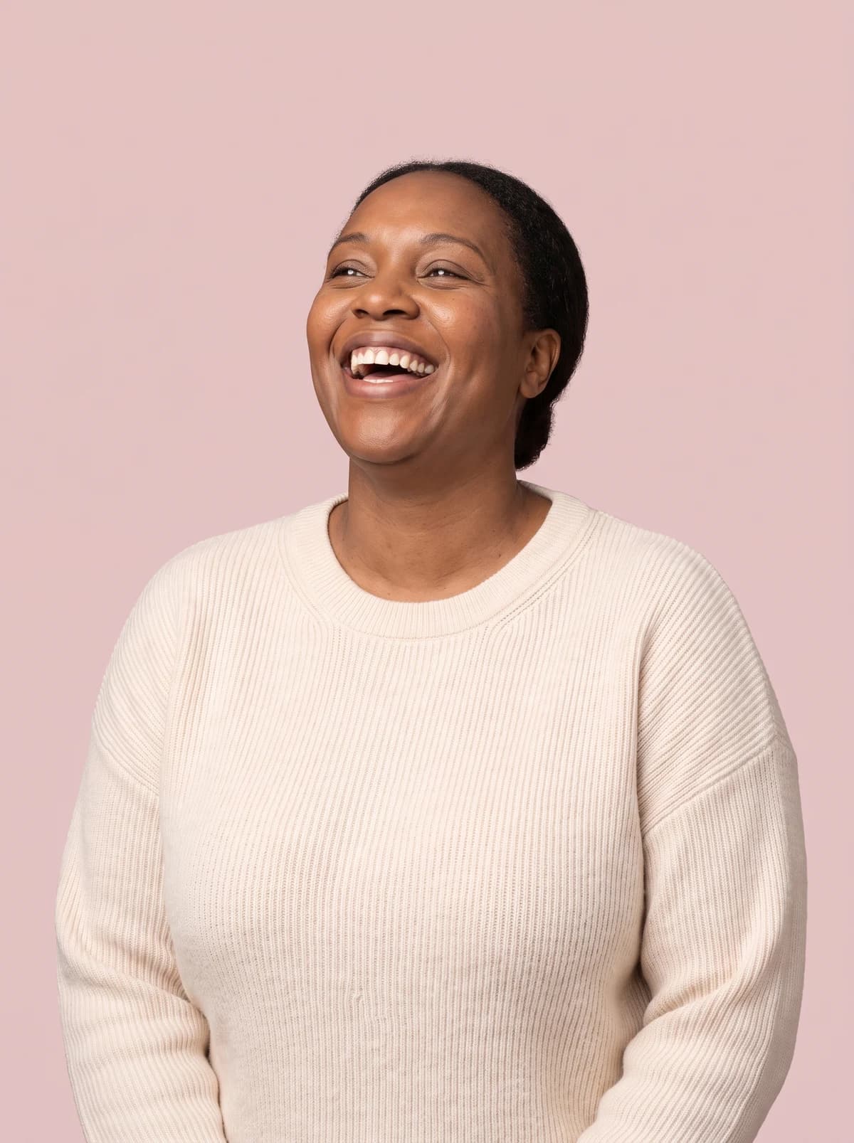 Woman laughing joyfully against a soft blush background.