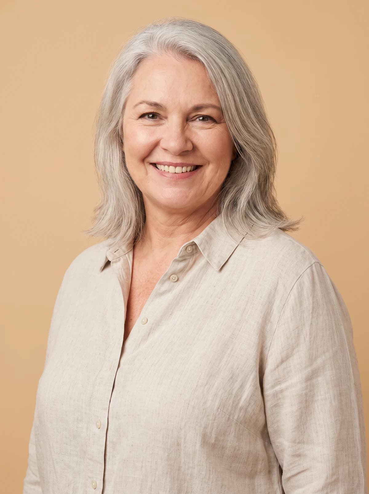 Silver-haired woman smiling warmly against a warm sand background.