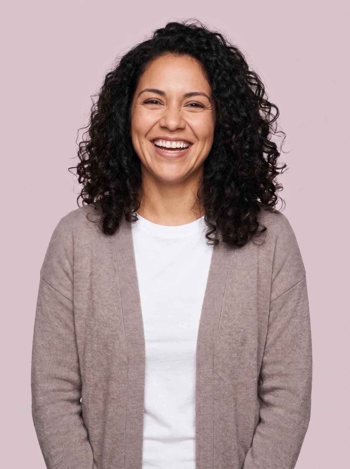 Woman with dark curls beaming against a pale mauve background.