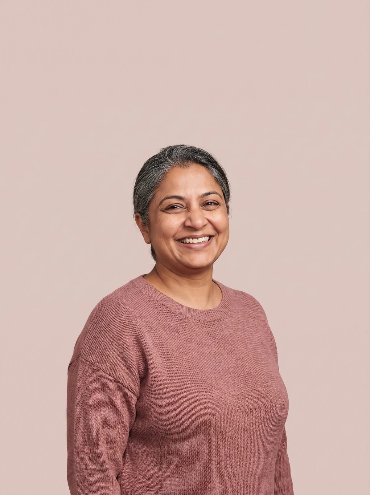 Woman smiling brightly against a soft rose-taupe background.